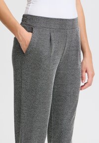 Hosen im Fischgrätmuster in Schwarz und Weiß, mit einem breiten Bund und Seitentaschen, aus einem glatten, strukturierten Stoff.