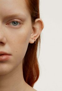 Pendiente de aro plateado con un pequeño acento de gema, llevado en el lóbulo, complementando la piel clara y el cabello rojizo. Primer plano de las características faciales.