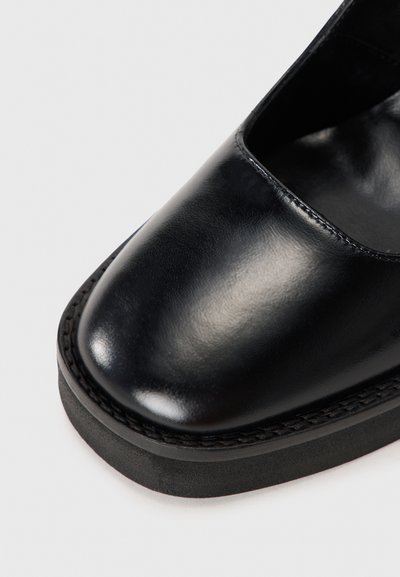 Pantofii negri din piele, cu vârf rotunjit, textură netedă și talpă plată neagră. Prezintă detalii de cusătură pe marginea tălpii.
