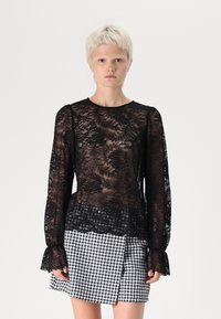 Black lace top with floral pattern, long sleeves, and ruffled cuffs, paired with a black-and-white houndstooth mini skirt.