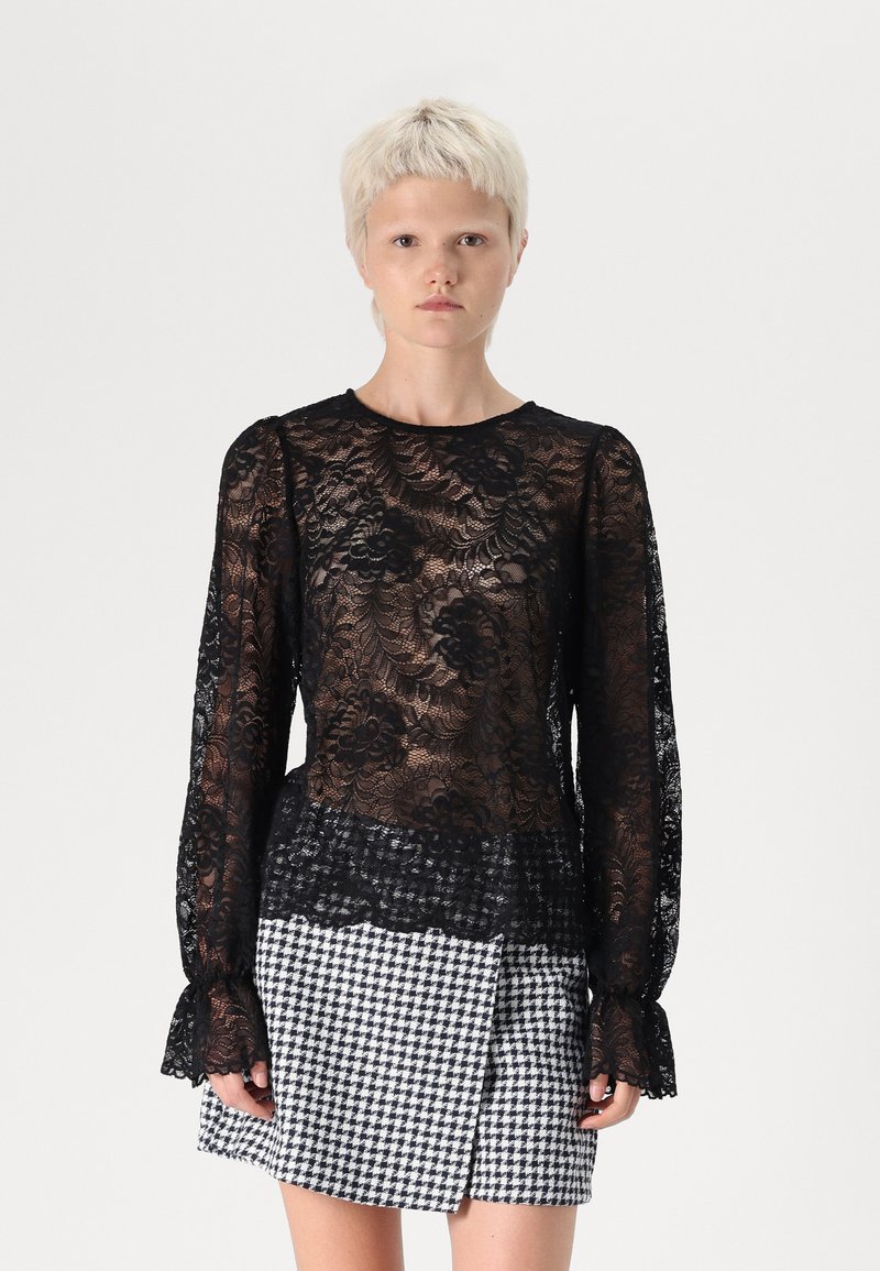 Black lace top with floral pattern, long sleeves, and ruffled cuffs, paired with a black-and-white houndstooth mini skirt.