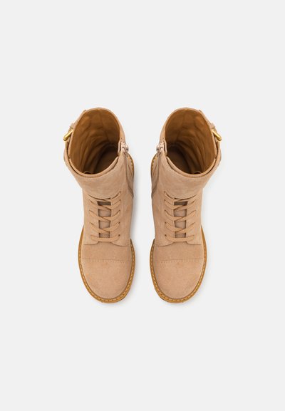 Bottes en suède beige avec un devant lacé, un bout arrondi et une tige repliable. Caractérisées par des détails en métal doré et une semelle en caoutchouc texturé.