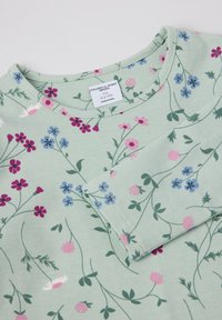 Vihreä pitkähihainen paita, joka on valmistettu pehmeästä kankaasta, jossa on kukkakuosi, jossa on vaaleanpunaisia, sinisiä ja purppuranvärisiä kukkia mintunvihreällä taustalla.