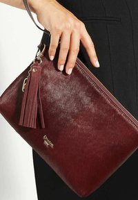 Burgundy leather clutch bag with a smooth texture, gold hardware, zipper closure, and a tassel accent. Handheld with a strap.
