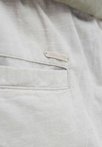 Svijetlosiva tkanina ima suptilnu teksturu s vertikalnom džepom i malom oznakom brenda ušivenom koja glasi "JACK & JONES."