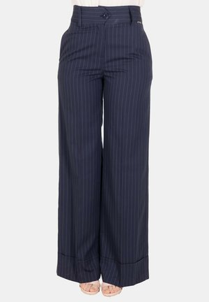 Pantaloni a gamba larga blu navy con sottili righe bianche, chiusura frontale con bottoni e orli risvoltati, indossati con sandali beige con punta aperta.