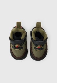 Groene stoffen peuterschoenen met zwarte accenten, gestructureerde zolen, verstelbare banden en trekflappen; met rode stiksels.