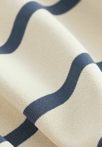 Woven fabric with cream base and dark navy wavy stripes. Soft texture with a consistent pattern, suitable for various textile applications.