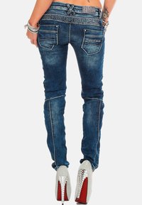 Jeans en denim bleu skinny avec une finition délavée, des coutures décoratives et deux poches arrière. Portés avec des chaussures à talons hauts argentées.