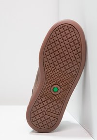 Suela de zapato Timberland marrón con tracción, logo hexagonal verde en el centro y texto "No marca" en el lado.