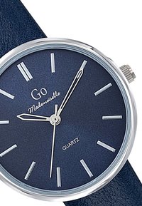 Montre à quartz avec un cadran bleu marine, aiguilles et index argentés. Boîtier en acier inoxydable argenté, bracelet en cuir bleu, design minimaliste.