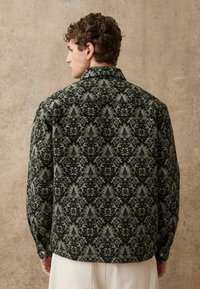 Dunkel gemusterte Jacke mit floralem Design in grünen und grauen Tönen, mit Kragen und detaillierten Knöpfen an den Ärmeln. Rückansicht dargestellt.