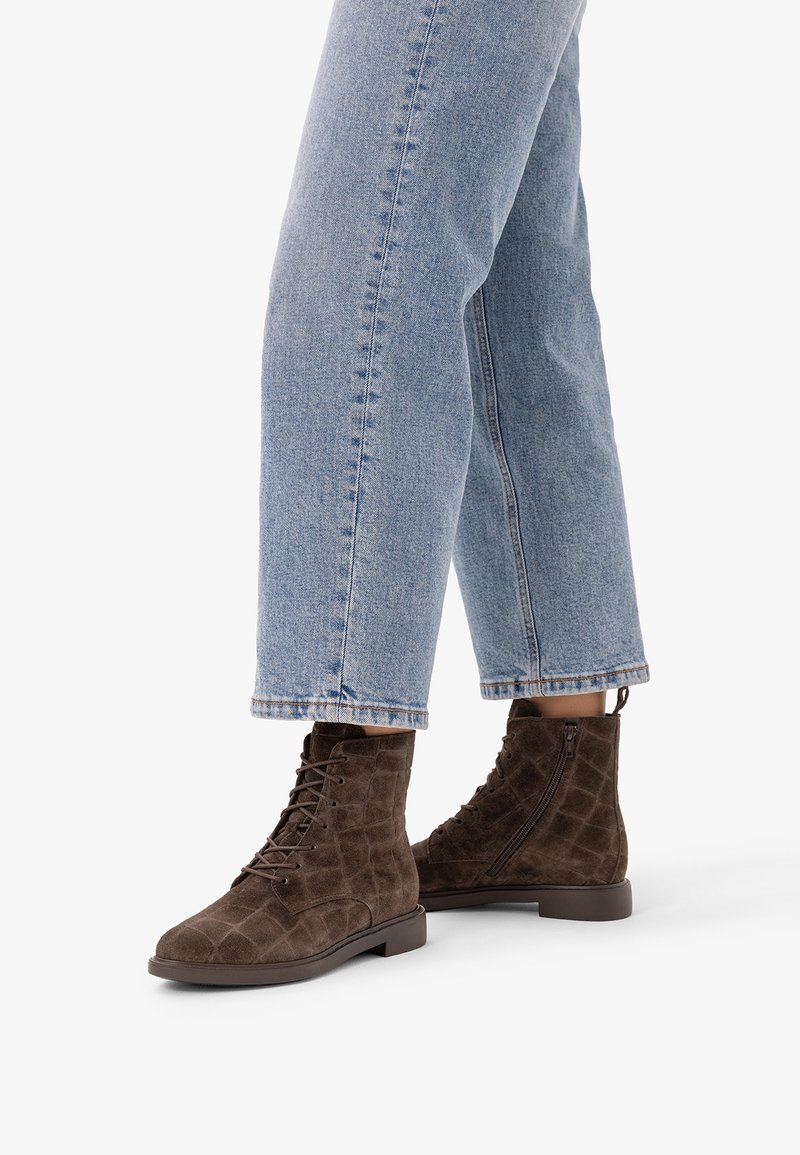Paire de bottines en daim marron à lacets avec fermetures éclair latérales, portées avec un jean droit bleu clair.