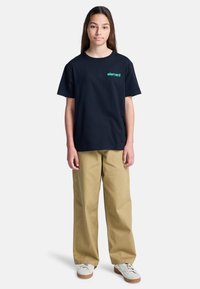 Czarny t-shirt z krótkim rękawem z logo "element" w kolorze zielonym, w połączeniu z beżowymi spodniami szerokimi w nogawkach i białymi trampkami z beżową podeszwą.