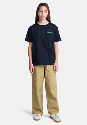 Czarny t-shirt z krótkim rękawem z logo "element" w kolorze zielonym, w połączeniu z beżowymi spodniami szerokimi w nogawkach i białymi trampkami z beżową podeszwą.