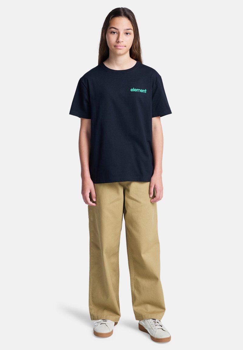 Czarny t-shirt z krótkim rękawem z logo "element" w kolorze zielonym, w połączeniu z beżowymi spodniami szerokimi w nogawkach i białymi trampkami z beżową podeszwą.