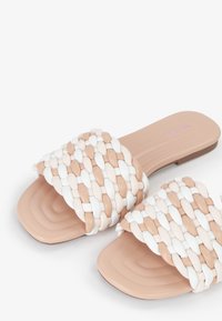Sandali a scivolo intrecciati con una fascia morbida e testurizzata in beige e bianco, con una suola interna solida marrone chiaro e un design a suola piatta.