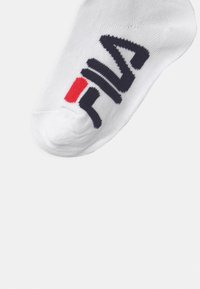 Hvite ankelstrømper med en marineblå "FILA"-logo med røde detaljer. Laget av et teksturert stoff som fremhever en tett passform og holdbarhet.