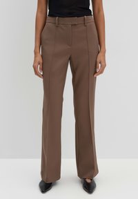 Pantaloni marroni a vita alta con una texture liscia, design a gamba dritta e dettagli sulle cuciture laterali. Abbinati a scarpe nere con punta a punta.