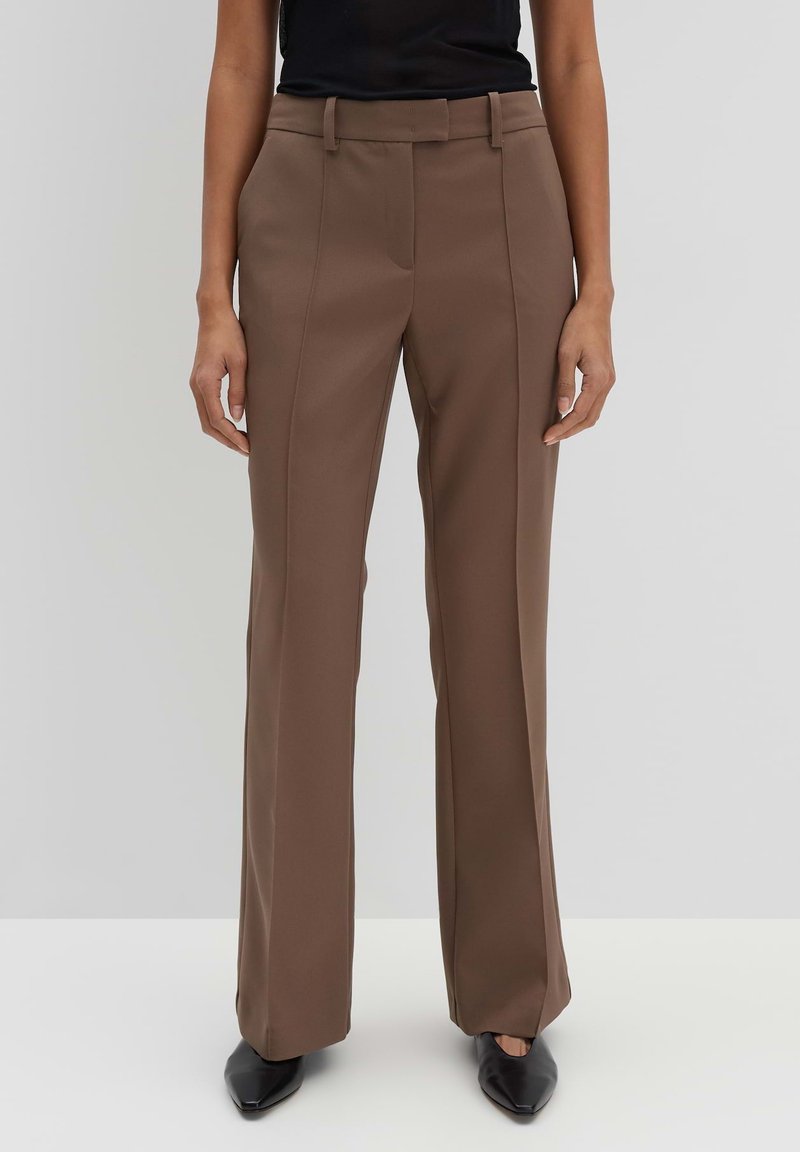 Pantaloni marroni a vita alta con una texture liscia, design a gamba dritta e dettagli sulle cuciture laterali. Abbinati a scarpe nere con punta a punta.