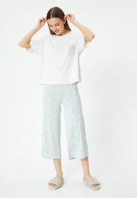 T-shirt blanc léger et à coupe décontractée avec une poche en mint à motifs, associé à un pantalon large à imprimé paisley mint et des chaussons gris.