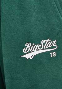 Žalias džemperis su minkšta tekstūra ir ryškiai balta "BigStar" logotipu su plačiu dizainu, šalia kurio yra skaičius "79".