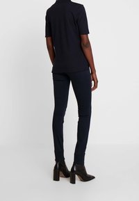 Polo negro de manga corta combinado con jeans ajustados de color azul oscuro y botas de tacón negro hasta el tobillo, mostrando una silueta elegante.