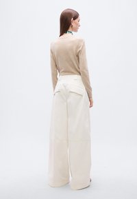 Μπεζ ελαφρύ πουλόβερ σε συνδυασμό με εκρού παντελόνι φαρδύ στο πόδι, με τσέπες μπροστά και πίσω. Λείο υλικό και μινιμαλιστικός σχεδιασμός.