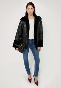 Černá kožená bunda s hebkým černým límcem a manžetami, v kombinaci se světle modrými úzkými džínami a vínovými botami na podpatku s špičatou špičkou.
