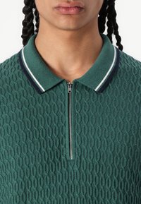 Polo shirt verde lavorato a maglia con motivo testurizzato, dotato di chiusura a zip e colletto con strisce bianche e blu navy.