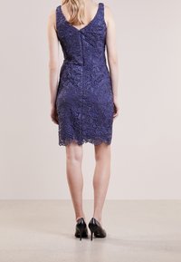 Marinblå spetsklänning med en åtsittande design, blommönster och scallopad nederkant. Bakdelen har en dold dragkedja och breda axelband. Svarta stilettklackar.