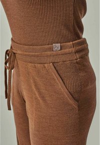 Brown loungewear set featuring ribbed texture, adjustable drawstring waist, and side pockets. Soft material with a fitted design.
