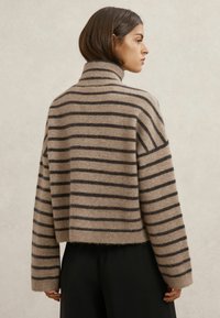 Beżowy sweter z dzianiny z ciemnobrązowymi poziomymi paskami, wysokim kołnierzem i krótkim krojem. Charakteryzuje się miękką teksturą i lekko postrzępionym dołem.