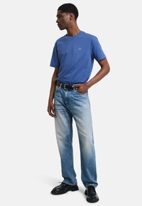 Blå bomulls t-shirt med rund halsringning, i kombination med ljus tvättade rakbenade jeans. Svart bälte och glansiga svarta skor fulländar looken.