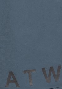 Donkergrijze letters "A", "T" en "W" gedrukt op een effen blauwe textielstof achtergrond.