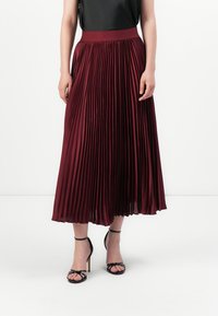 Burgundy pleated maksi-hame, jossa on joustava vyötärö, valmistettu sileästä ja valuista kankaasta. Yhdistetty mustiin remmisandaaleihin.