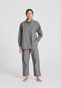Camicia button-up in cotone grigia con maniche lunghe e taschino, abbinata a pantaloni a gamba larga grigi coordinati. Entrambi i capi hanno una vestibilità comoda.