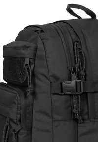 Black backpack made of durable fabric, featuring zippered compartments, a mesh side pocket, and a plastic buckle. Reinforced stitching for strength.