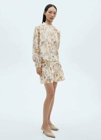 Floral-patterned blouse in light fabric, featuring long sleeves and a high neckline, paired with a matching knee-length skirt and nude heels.