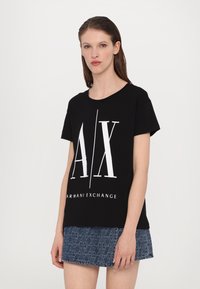 Čierne bavlnené tričko s bielym logom "AX" a textom "ARMANI EXCHANGE". Má krátke rukávy a voľný strih. Skombinované s džínovou sukňou.
