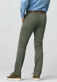 Olivgrüne Baumwollhosen mit schmalem Schnitt, zwei Gesäßtaschen und einem gemusterten Gürtel. Kombiniert mit lässigen Sneakers.