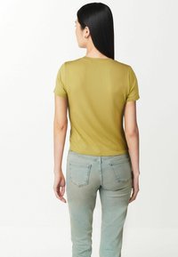 T-shirt verde oliva a maniche corte con un design aderente, texture a coste e scollatura rotonda, abbinato a jeans azzurri chiari.