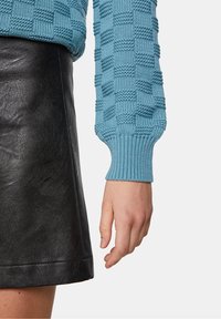 Pull texturé bleu clair avec un motif de tricot à carreaux, associé à une mini-jupe en cuir noir. Mise en avant des détails de la manche et de la main.