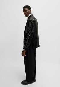 Schwarzer Pailletten-Blazer mit langen Ärmeln, taillierter Passform und einem eleganten Design, kombiniert mit schwarzen weit geschnittenen Hosen und Plateauschuhen.