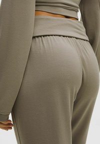 Szürke, rugalmas anyagú melegítőnadrág, magas derékkal, bordázott részletekkel és laza szabással. Simább textúra és diszkrét tonális szín.