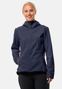 Giacca softshell blu navy con design aderente, zip completa e cappuccio. Presenta tasche laterali e un logo discreto sul petto. Texture liscia.