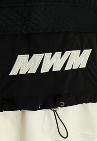 Tela negra con letras blancas bordadas "MWM" y un cordón ajustable negro con tope de metal sobre tela blanca.