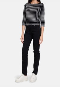 Randig svart och vit trekvartsärmad skjorta i kombination med svarta jeans och vita sneakers. Tyget verkar mjukt och åtsittande.