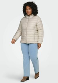 Bēšs pūkains jaka ar rāvējslēdzēja priekšpusi un kapuci, ar šūtu rakstu. Valkāta kopā ar gaismi zilām džinsām un brūnām papēžu zābakiem.