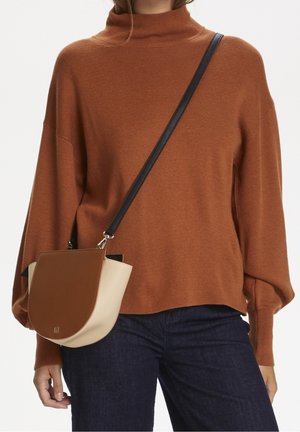 Femme portant un pull à col roulé marron et un jean foncé avec un sac bandoulière marron et beige avec une sangle noire.